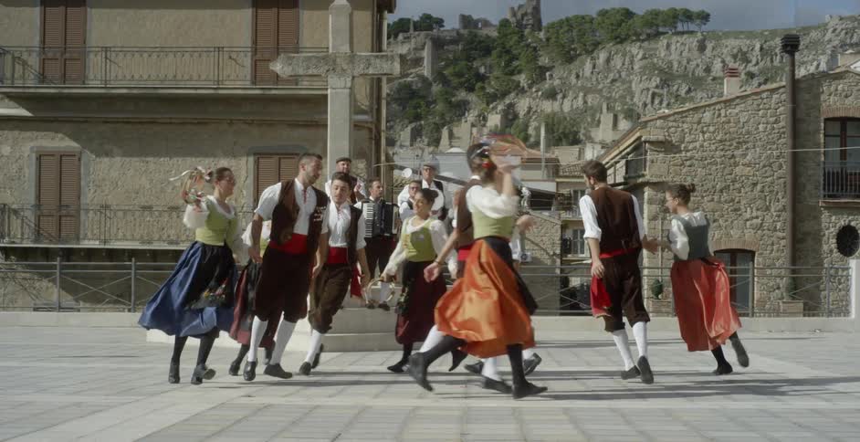 People in costumes are doing a traditional dance outside in daylight