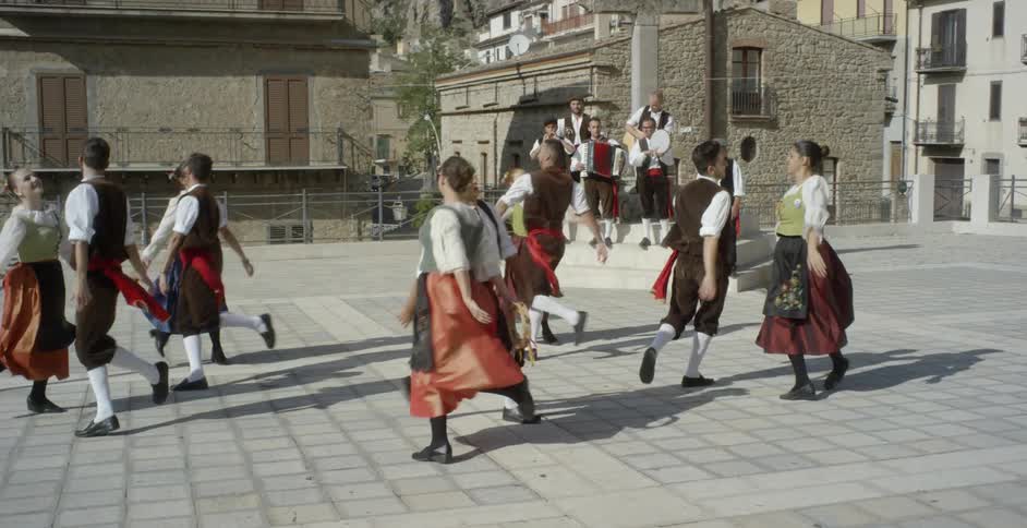 Men and women dance to a live band in unison in a city square