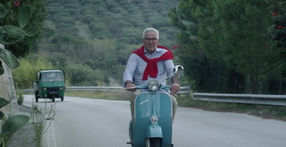 Old man navigates scooter along winding mountain road