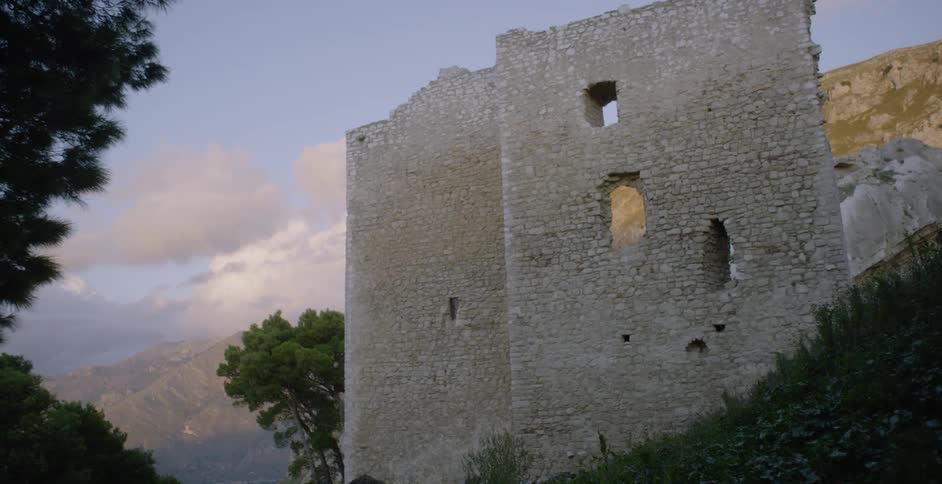 An abandoned stone building sits near mountains