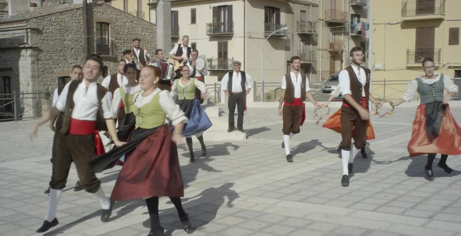 Performers dance outside in a village