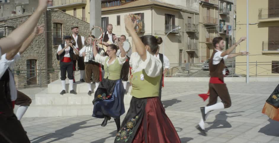 People in costumes are doing a traditional dance outside in daylight