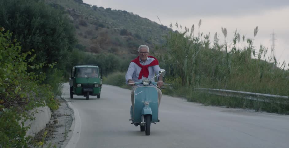 Old man navigates scooter along winding mountain road