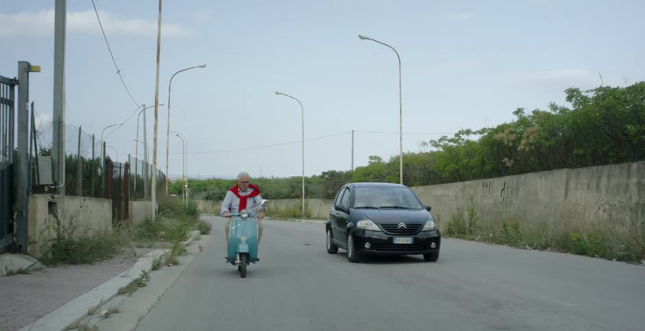 A car drives by a man riding a scooter