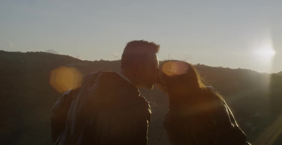 A couple taking in a view during the day are leaning in to kiss