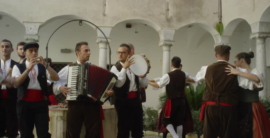 Couples in costume dance around musicians in a courtyard