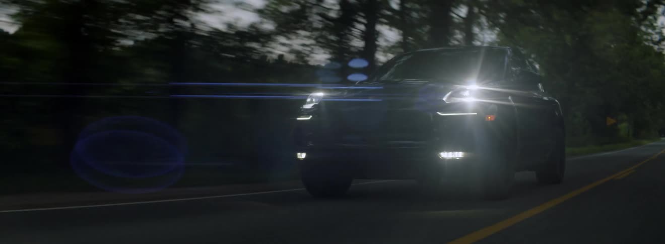 A vehicle is driving on a rural road with its lights on at dusk