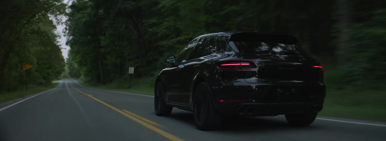 A black car travels on a tree lined road