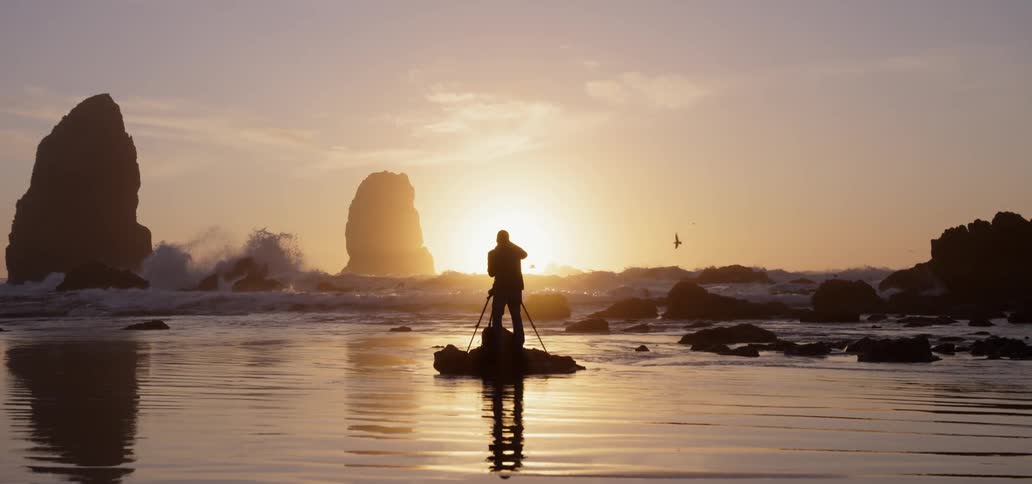 A man photographs a beach at sunset