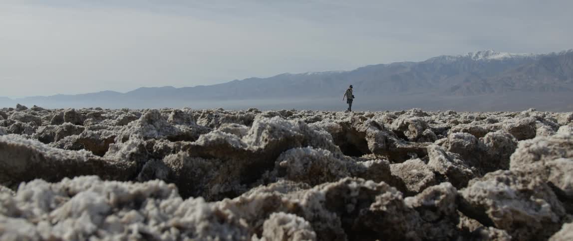 A person carrying a camera is walking over a field of rocks in daylight