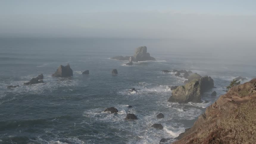 Waves are lapping a rugged coastline on a foggy day