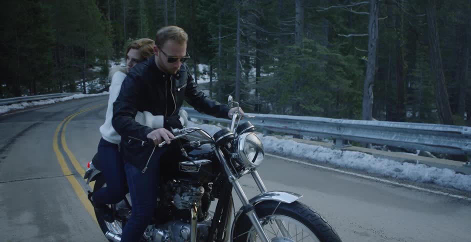 A woman holds onto a man on a motorcycle stopped in the road