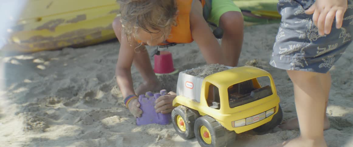 Two children are playing in the sand on a beach during the day