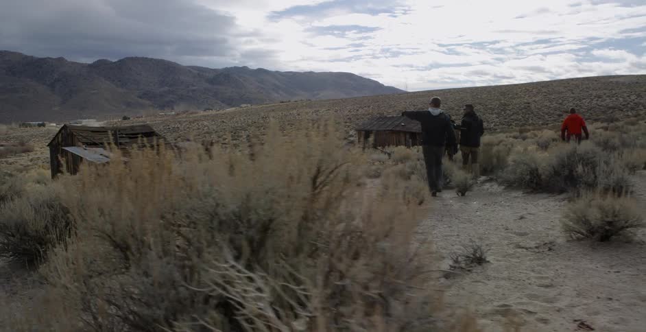 A group of friends are hiking towards abandoned buildings in the desert in daylight