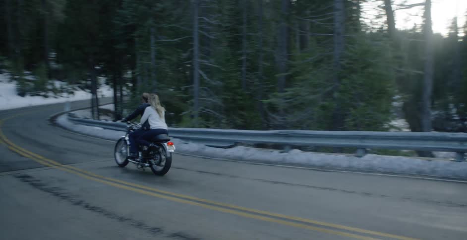 A man and woman ride a motorcycle through a forest