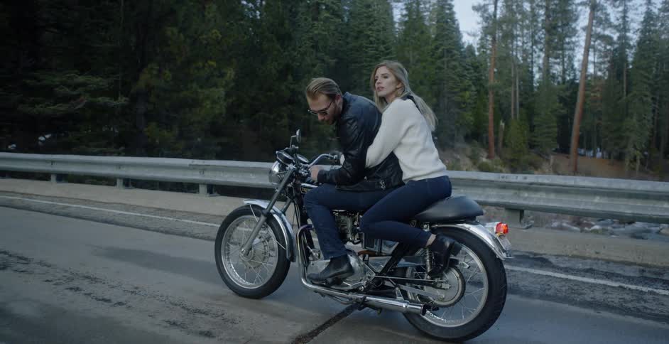 A man and woman ride a motorcycle in a forest