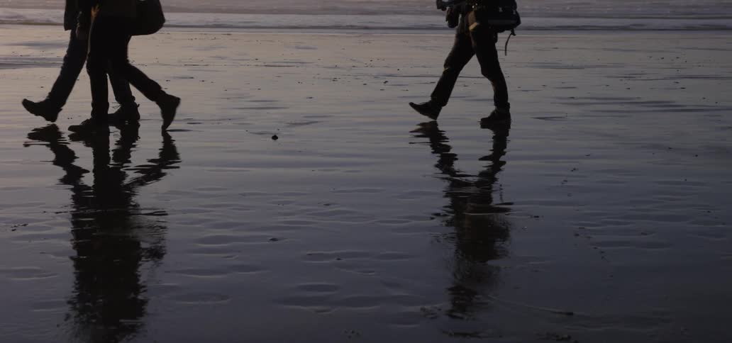 People carry bags and backpacks are reflected on the wet sand