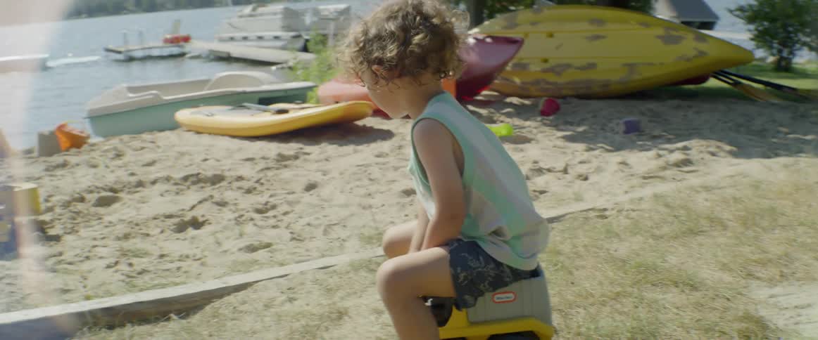 Small boy rides toy truck near lake