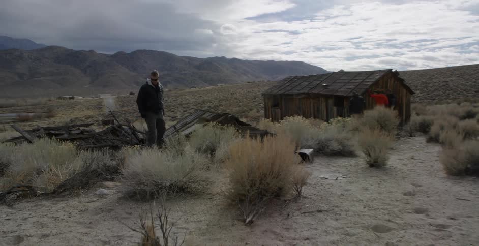 A man examines wood near an abandoned shack in the desert