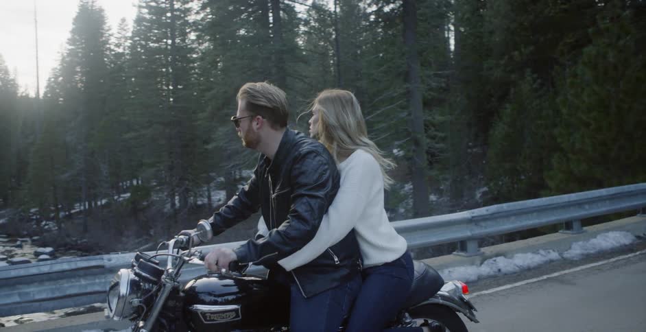 A man and woman ride a motorcycle in a forest