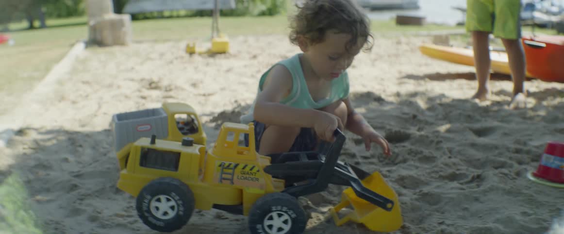 Child on the beach plays with sand toys on a cloudy day as another walks away behind him