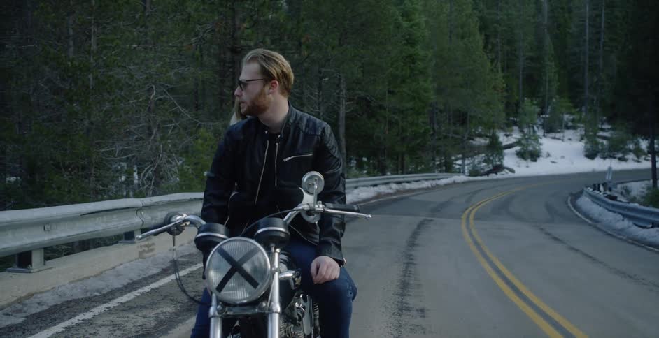 A man and woman ride a motorcycle in a forest
