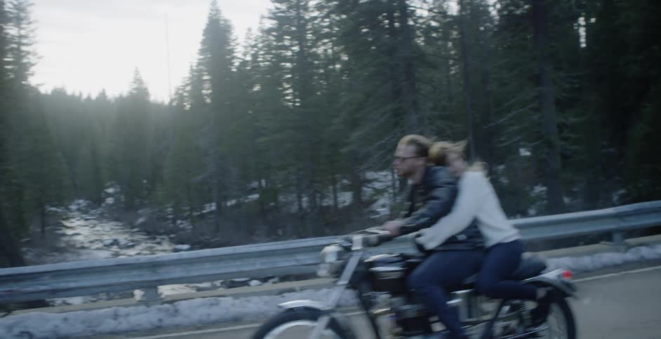 A man and woman ride a motorcycle down a mountain road