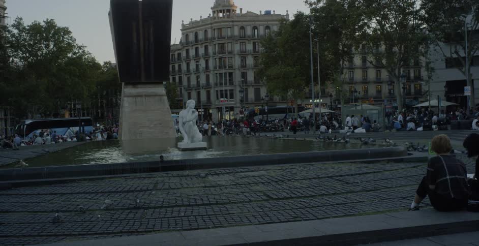 Birds fly up from a pool of water in a city square with many people around