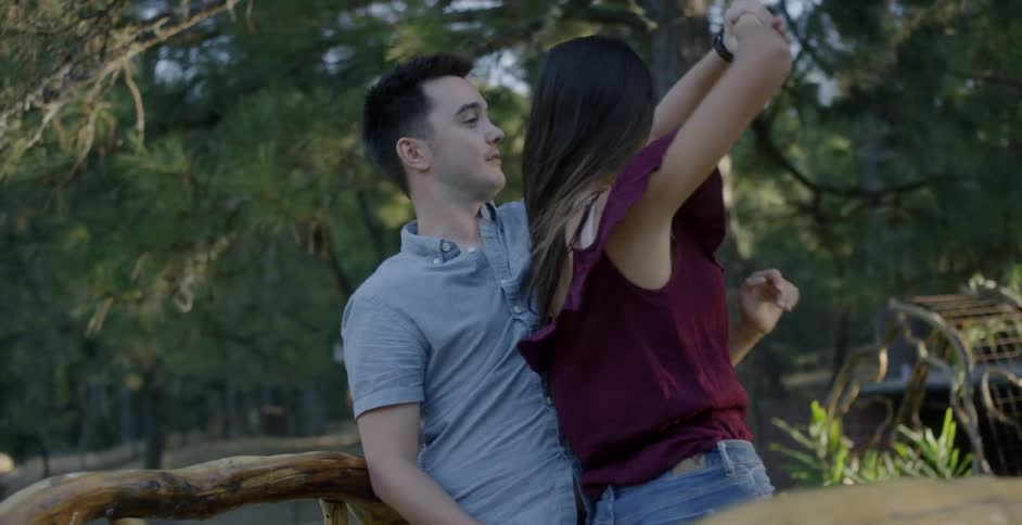 A man and woman dance outside under the trees