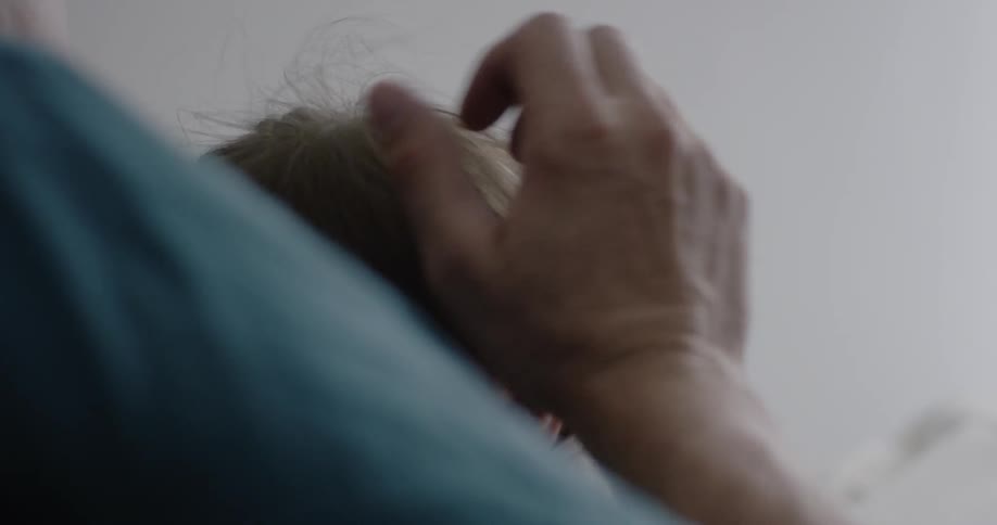 A man is rubbing the head of his baby as they sit on a bed