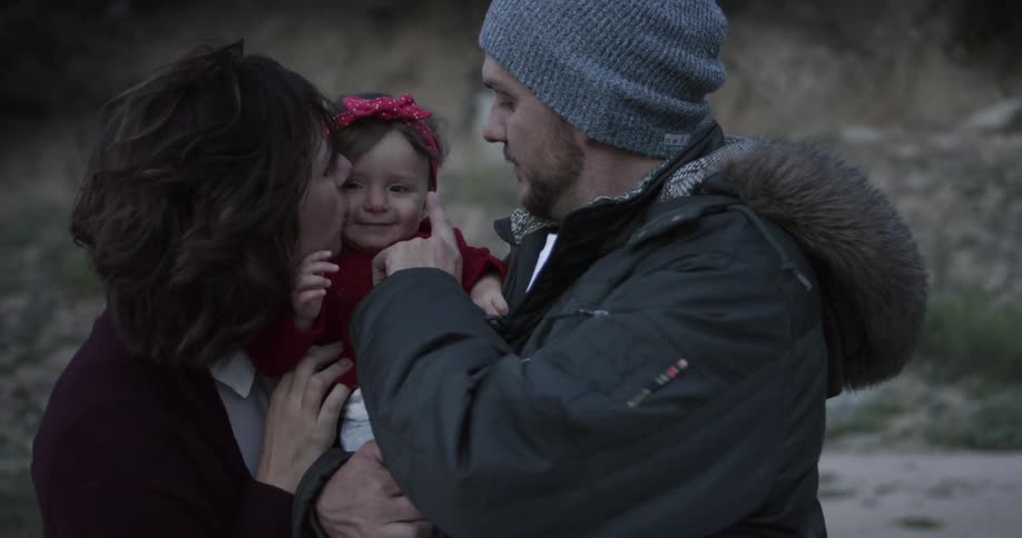 A man and woman kiss a baby outside