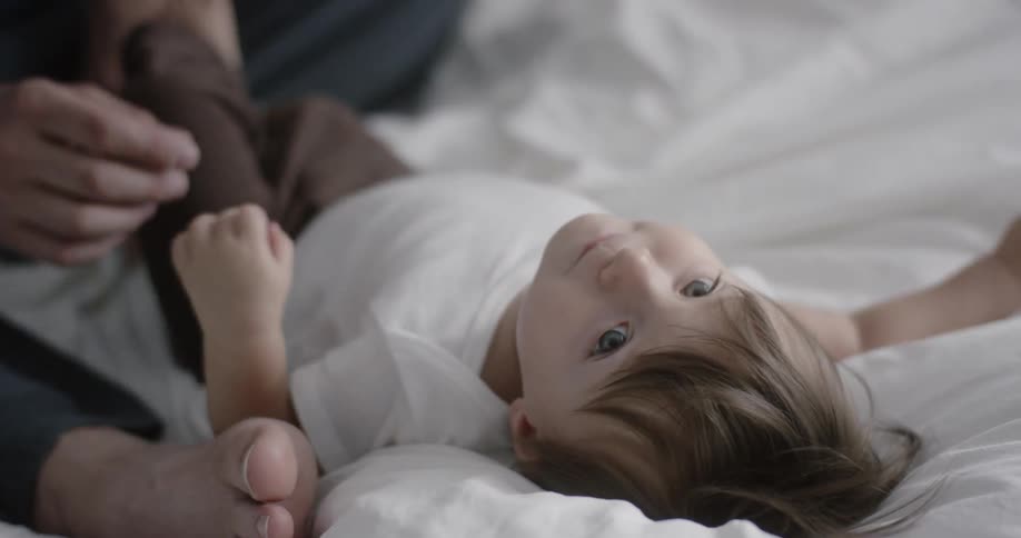 A dad rubs his son's belly while he lies on a bed