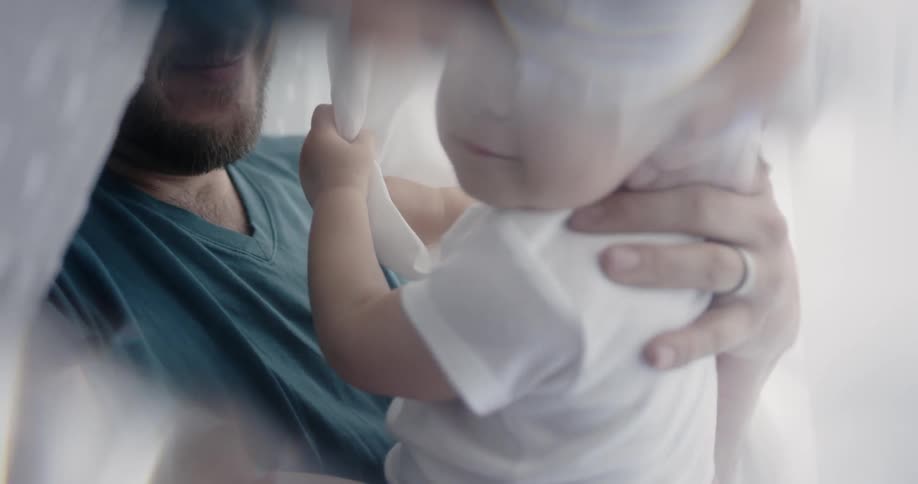 Bearded man holding an infant with fabric hanging around them