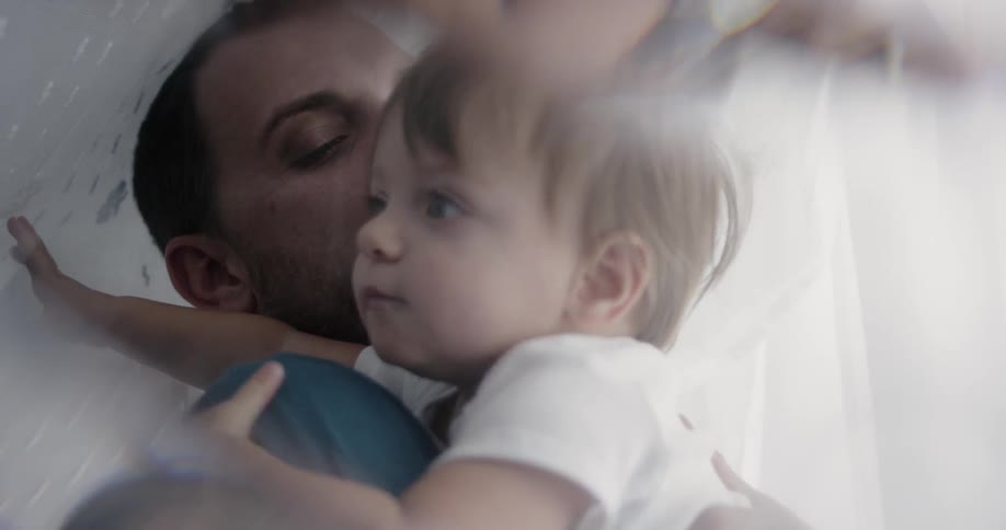 A child is laying down with a man in bed
