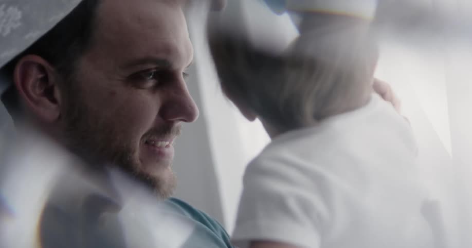 A man smiles as he plays with his baby in a room during the day