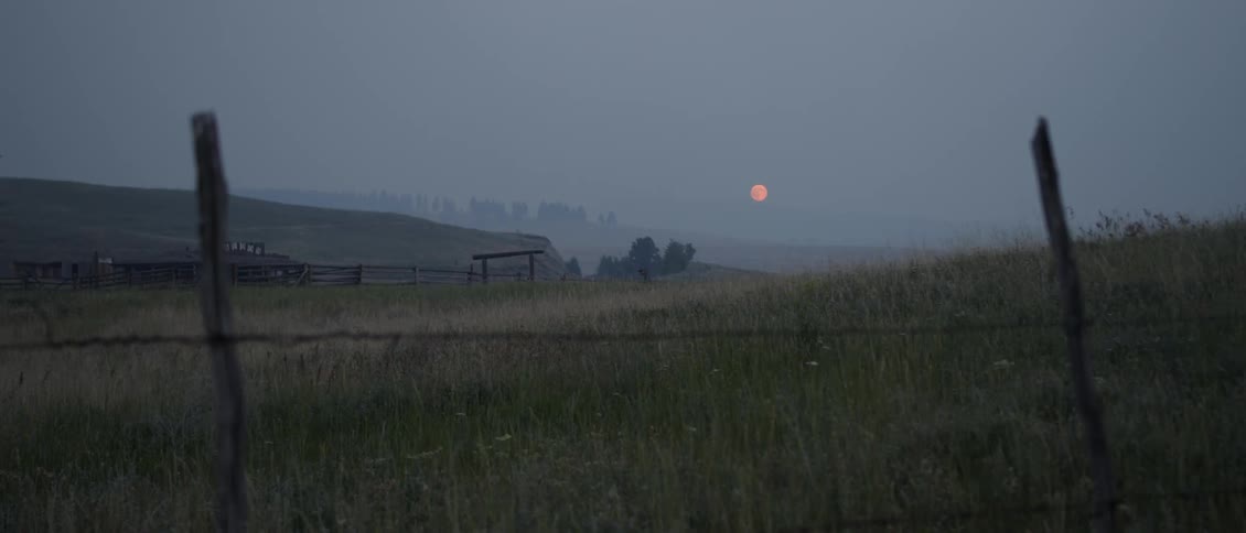 The moon is rising over farm land with a large city in the background