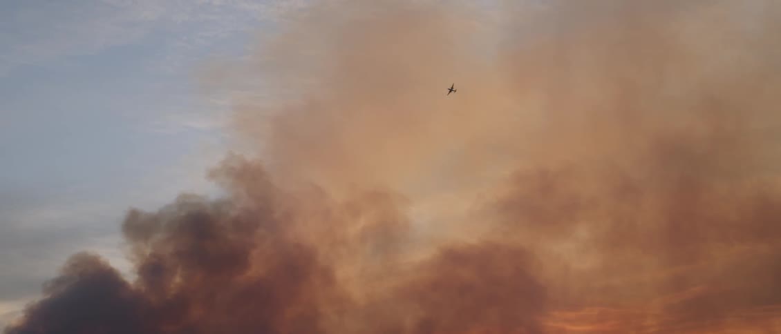 An airplane flies in a smoky sky at sunset