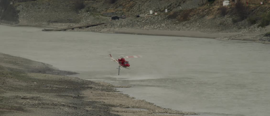 A red helicopter is filling up its tank with water at a small river