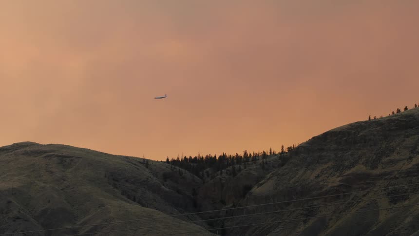 A plane flies over the mountain at sunset