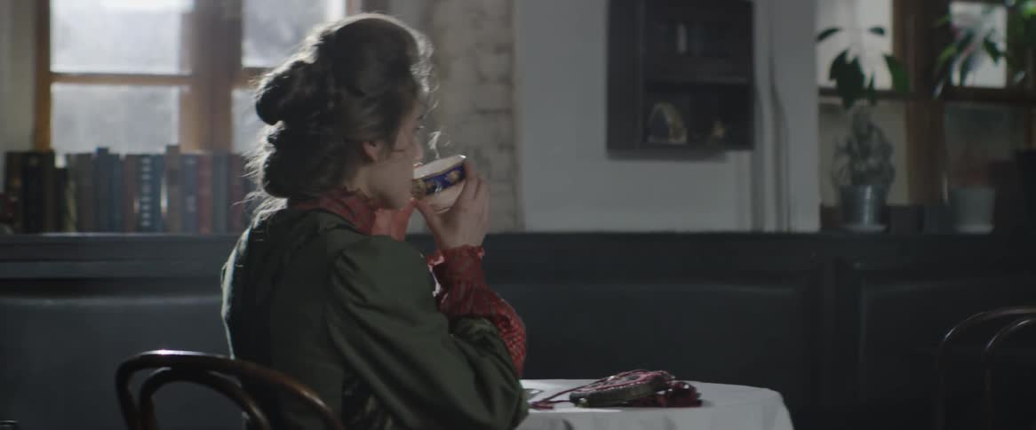 A woman sits at a table and takes a drink