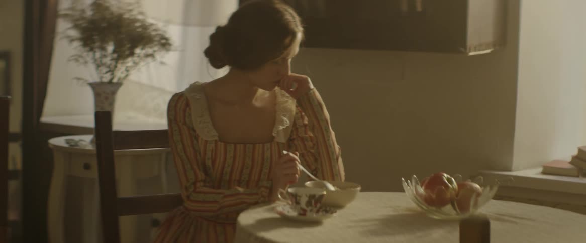 A woman sits at a table with tea and fruit