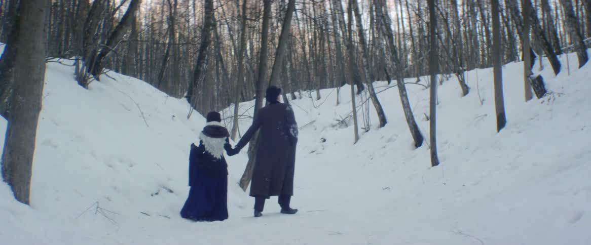 A man and woman hold hands while walking in a snowy forest