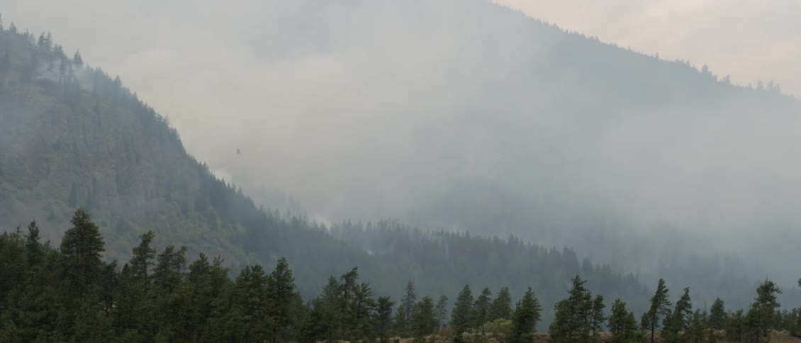 The helicopter dumps water over the fire on the hills
