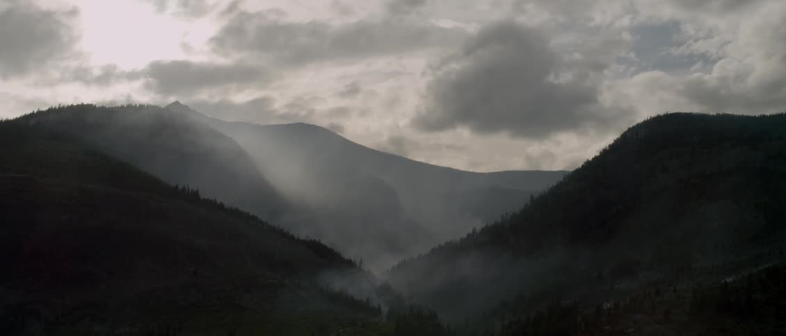 Smoke pours from the valley between mountains