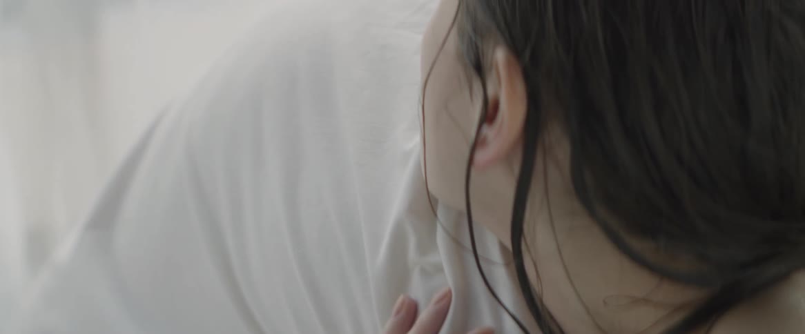 Woman puts her face on a white sheet on a bed