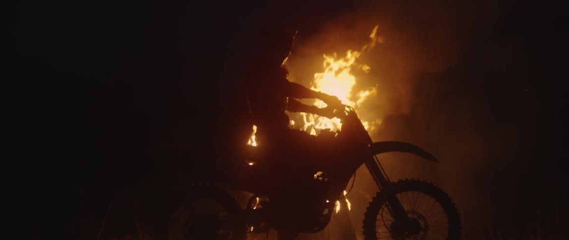 A dirt bike rider stops in front of a bonfire