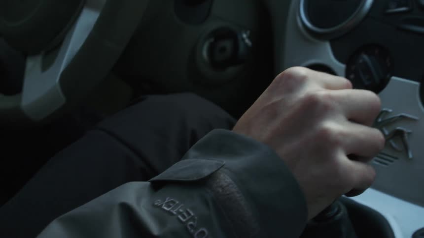 A man is shifting gears as he drives a car in daylight