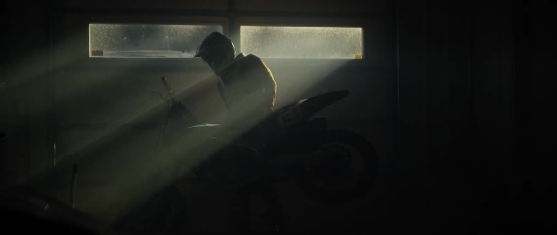 A man is lifting a dirt bike and rolling it out of a garage