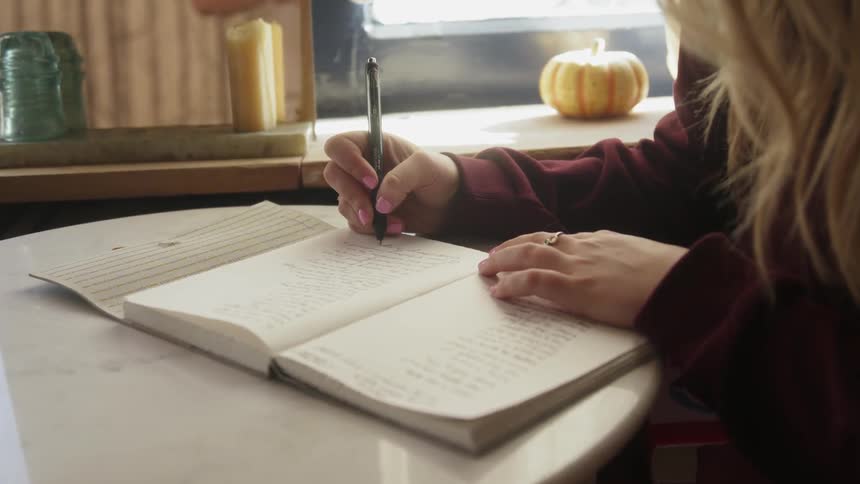 A woman writes in a notebook at a small table