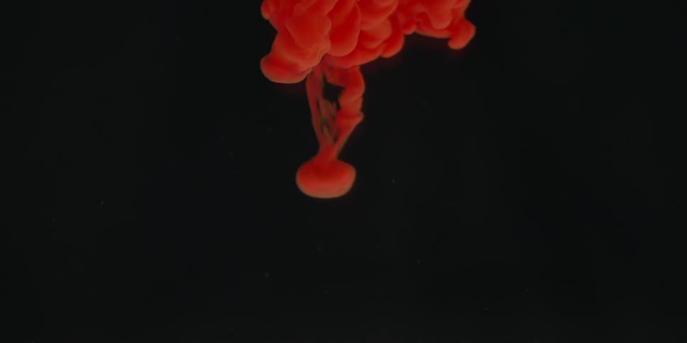 A cloud of red colored dye is billowing and falling into a clear liquid